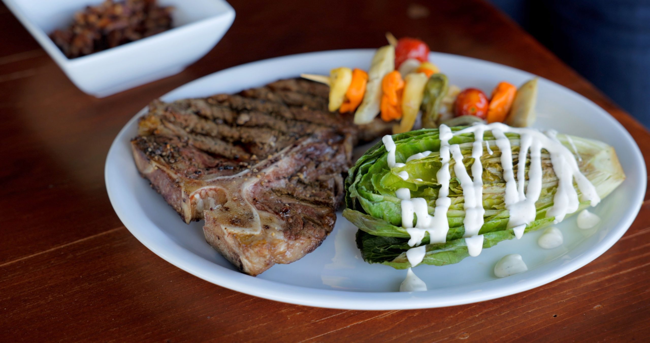 A grilled T-Bone Steak with pasta salad and grilled romaine